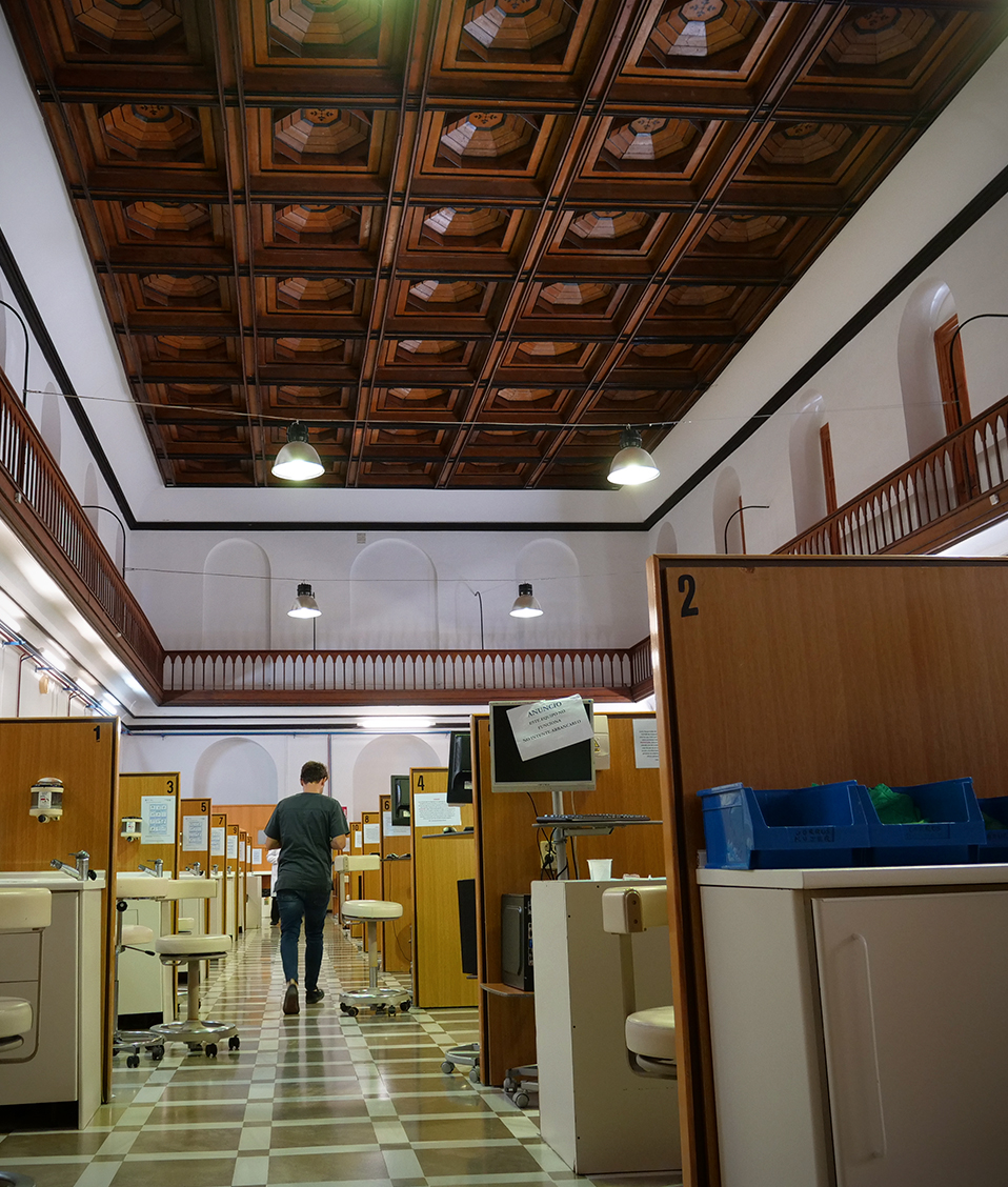 Estudiante caminando por un pasillo entre las sillas dentales separadas por cubículos en una gran sala de la Facultad de Odontología