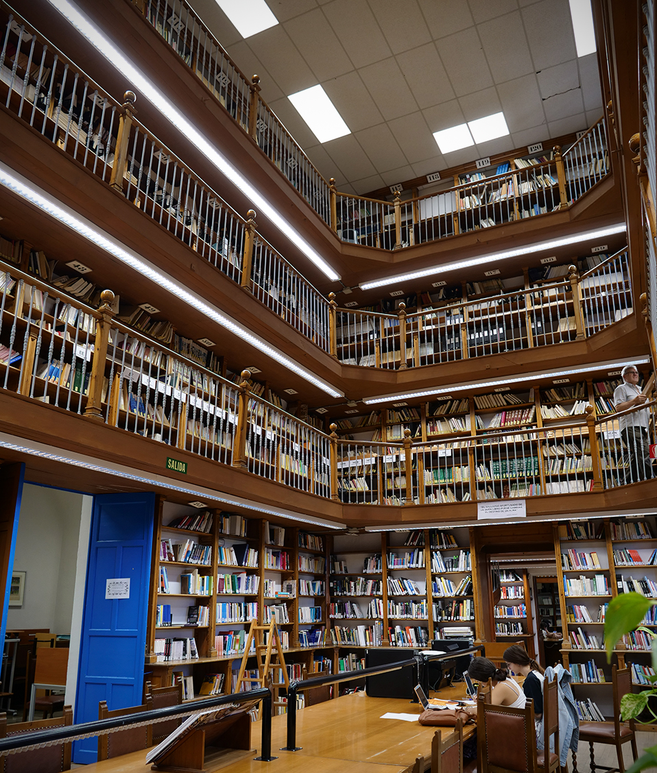 Biblioteca de la Facultad de Comunicación y Documentación de cuatro plantas de estanterías con libros y mesas de estudio en la planta baja