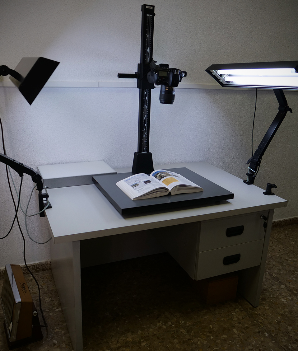 Mesa con dos focos laterales y una cámara central enfocando a un libro abierto