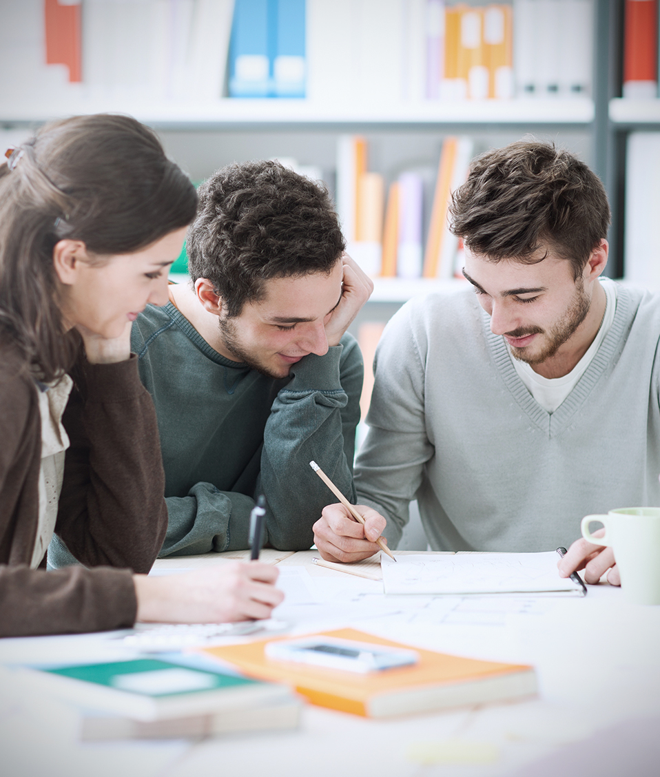 Tres estudiantes en una mesa de estudio de una biblioteca comparando sus apuntes